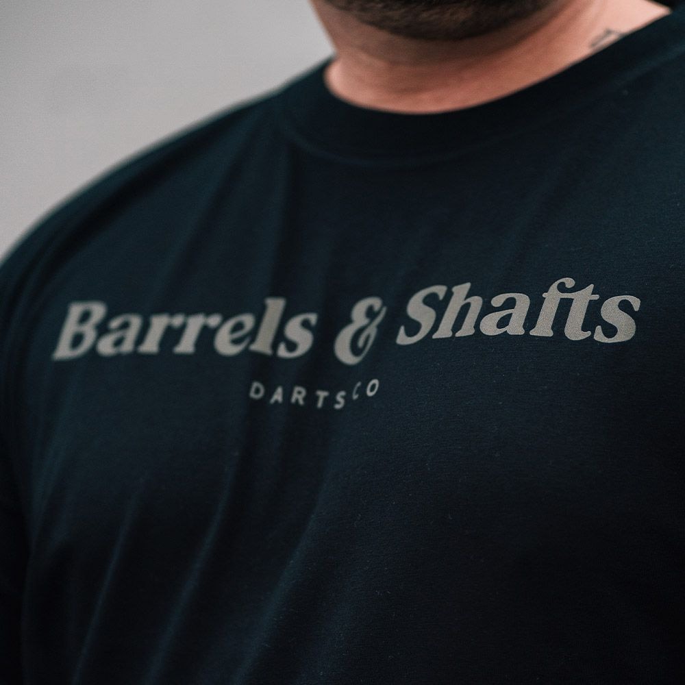 T-Shirt Barils et Arbres - Noir Das Bild zeigt ein schwarzes T-Shirt mit der Aufschrift "Barrels & Shafts". Darunter steht in kleineren Buchstaben "DARTSCO".