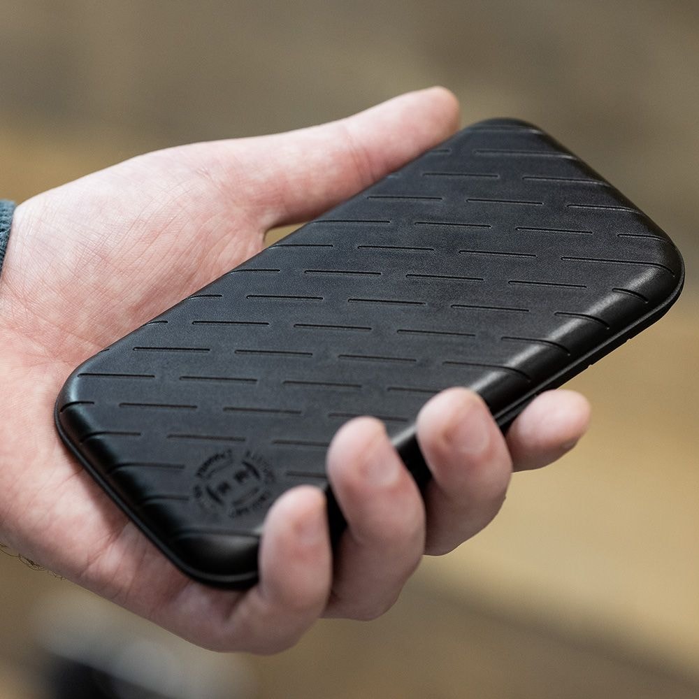 Étui à fléchettes Harrows Slimcase Eine Person hält eine schwarze, schlanke Darttasche in der Hand. Die Oberfläche der Tasche hat ein dezentes, gerilltes Muster.