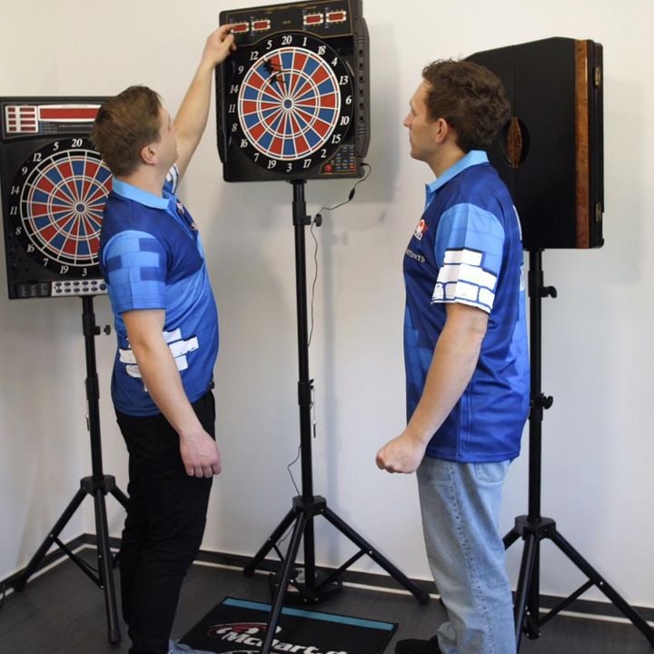 CB50 Zwei Männer in blauen Shirts stehen vor elektronischen Dartscheiben. Einer der Männer nimmt einen Dartpfeil aus der Dartscheibe.