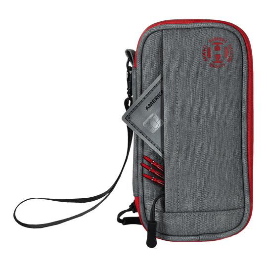 Étui intelligent Harrows pour fléchettes Das Bild zeigt ein graues und rotes Dart-Etui mit einem Reißverschluss und einer Handschlaufe. In der Vordertasche stecken eine Kreditkarte und einige Dartspitzen.