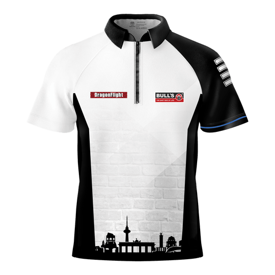 Das Bild zeigt das Bulls Martin Schindler The Wall Dartshirt mit einem schwarz-weißen Design und kurzen Ärmeln. Auf der Vorderseite befinden sich Logos und eine stilisierte Stadtsilhouette am unteren Rand.