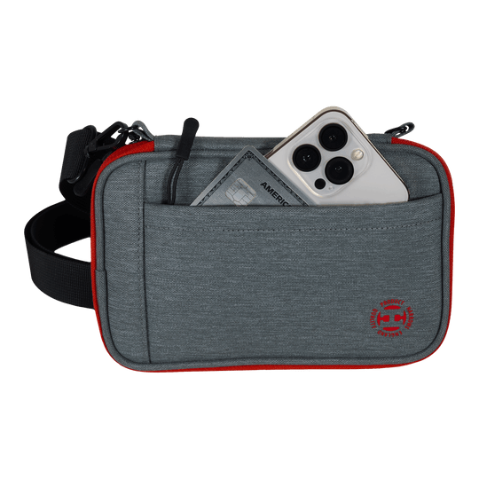 Portefeuille à fléchettes Harrows Smart Case XL Das Bild zeigt eine graue Tasche mit rotem Rand und einem schwarzen Gurt. In der Vordertasche stecken ein Smartphone und eine Kreditkarte.