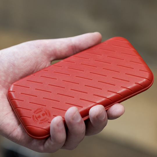 Eine Person hält eine rote, strukturierte Darttasche in der Hand. Die Darttasche hat eine schlanke und kompakte Form.