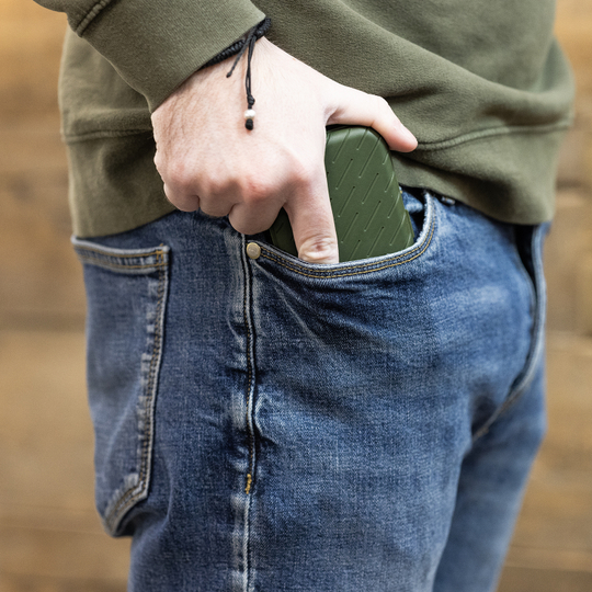 Étui à fléchettes Harrows Slimcase Eine Person steckt ein grünes Etui in die vordere Hosentasche einer Jeans. Das Etui hat eine strukturierte Oberfläche und passt gut in die Tasche.