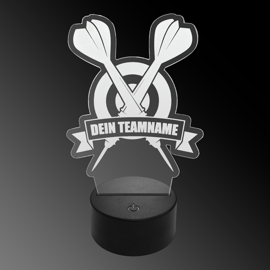 Lampe à fléchettes LED en plexiglas avec texte personnalisé Das Bild zeigt eine LED-Lampe aus Plexiglas in Form von zwei gekreuzten Dartpfeilen vor einer Zielscheibe. Auf einem Banner steht der Text "DEIN TEAMNAME".